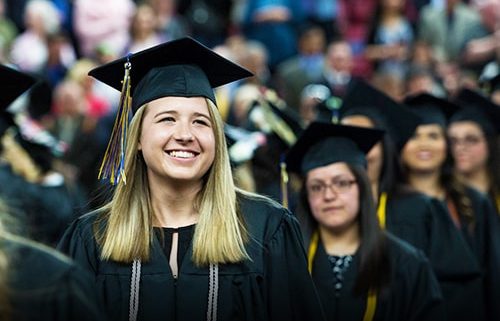 Student smiling looking up at crowd in graduation outfit