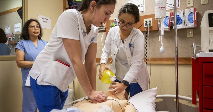 A female nursing student holds up a beaker and examines the contents.