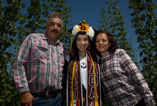 DACA Student at Heritage University poses for graduation picture with parents.