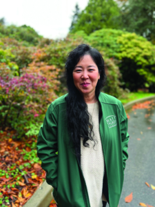 Portrait of a woman with long black hair wearing a white top and green jacket outside