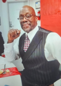 Close-up of a man with glasses wearing a long white sleeve and a black vest