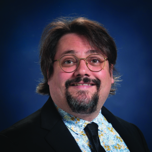 Headshot of a man with a goatee and glasses wearing a shirt and tie