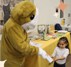 A person in a mascot costume hands a book to a child