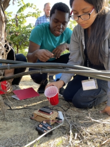 A man and a woman working on a device with batteries with the woman pouring water on the device.