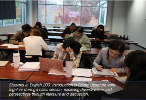 Photograph of a classroom with students seated at desks, engaged in collaborative work during an English 200: Introduction to Ethnic Literature session. Students use notebooks, laptops, and writing materials, highlighting active discussion and diverse perspectives in literature studies.