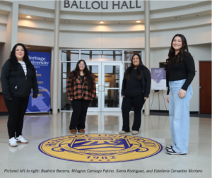 Photograph of four women standing inside Ballou Hall at Heritage University, positioned around a large university seal on the floor. The setting includes a blue university banner and a signboard in the background, highlighting a campus environment. 