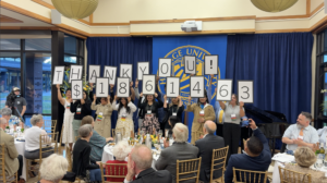 Photograph of a group of people standing on a stage holding signs that spell out 