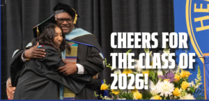 Photograph of a graduation ceremony showing a graduate in a black cap and gown hugging a faculty member in academic regalia. White text on the right side reads "Cheers for the Class of 2026!" with colorful flowers and a blue and yellow emblem partially visible in the background.