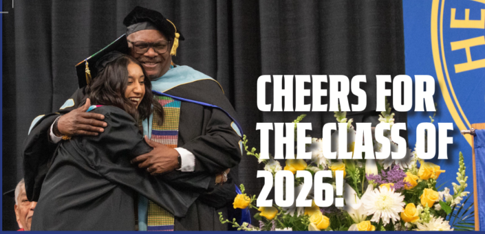 Photograph of a graduation ceremony showing a graduate in a black cap and gown hugging a faculty member in academic regalia. White text on the right side reads "Cheers for the Class of 2026!" with colorful flowers and a blue and yellow emblem partially visible in the background.