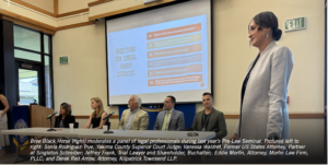 Photograph of a panel discussion moderated by Bree Black Horse during a Pre-Law Seminar, featuring legal professionals seated in a room with a projection screen displaying a slide titled "Questions for Small Group Exercise." The slide contains six numbered questions in orange and white text on a blue background, focusing on legal topics and professional experiences.